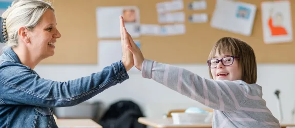 Ein behindertes Kind und die Lehrkraft geben sich die Hand
