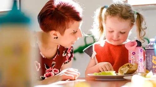 Erzieherin hilft Krippenkind beim Essen
