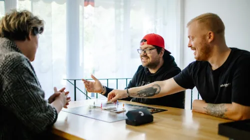 Drei Menschen spielen an einem Tisch ein Spiel.